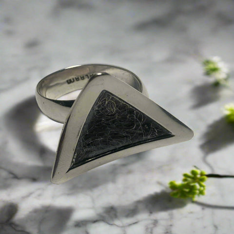 Triangular silver ring with textured center on a marble surface